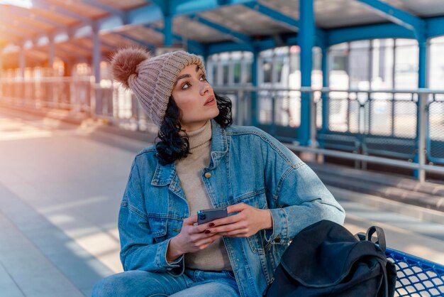A woman in a denim jacket is talking on the phone and waiting for a tram at the stop Lifestyle photo