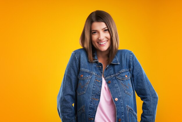 Foto donna in giacca di jeans che guarda l'obbiettivo su sfondo giallo