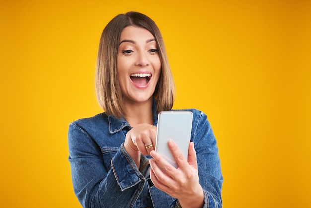 woman in denim jacket with smartphone over yellow background