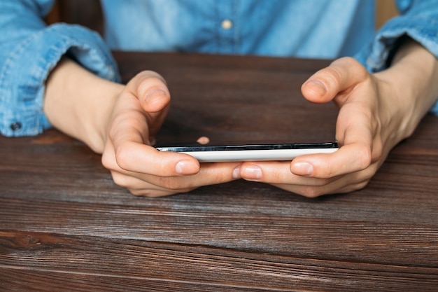 Woman in a denim shirt holding a cell phone and sitting behind a wooden table