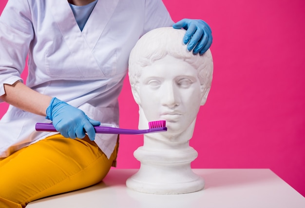 Foto dentista della donna che lava i denti di una statua antica usando un grande spazzolino da denti