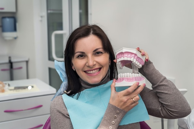 Woman in dentist chair holding jaw and smiling