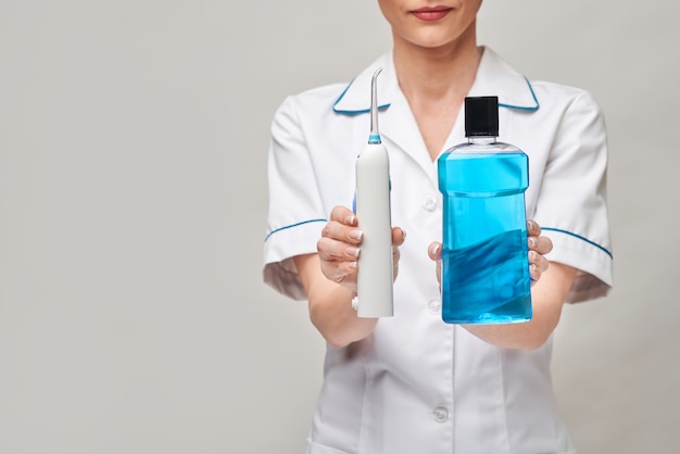 Woman dentist doctor holding bottle of mouthwash and irrigator.