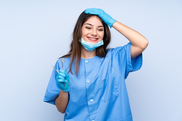 Woman dentist holding tools over blue wall laughing