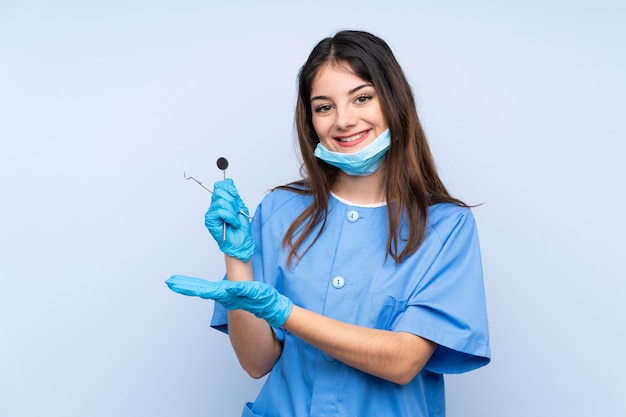 Woman dentist holding tools over isolated blue wall holding copyspace imaginary on the palm