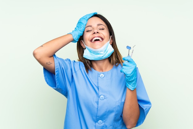 Woman dentist holding tools over isolated green wall laughing