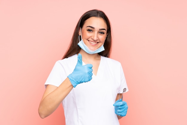 Gli strumenti di tenuta del dentista della donna isolati sulla parete rosa dare pollici aumentano il gesto