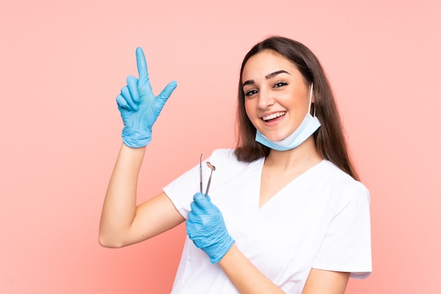 검지 손가락으로 가리키는 분홍색 벽에 고립 된 도구를 들고 여자 치과 의사 좋은 아이디어