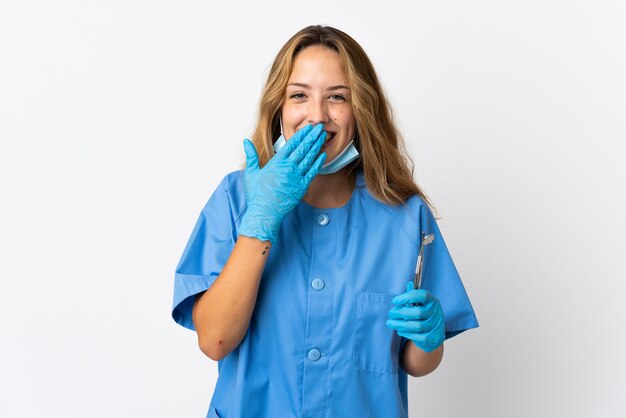 Woman dentist holding tools isolated on white happy and smiling covering mouth with hand