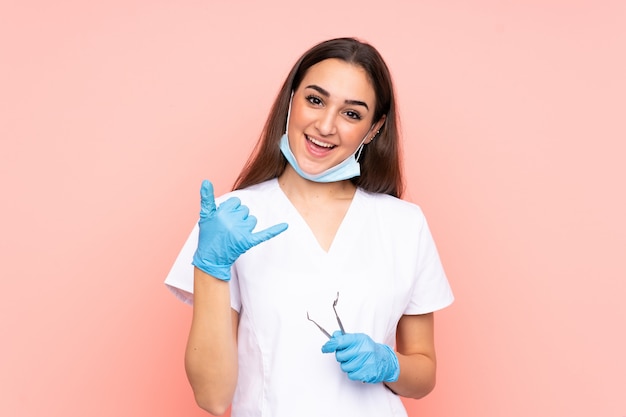 Woman dentist holding tools on pink making phone gesture