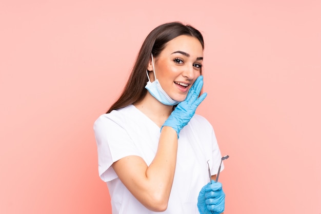 Woman dentist holding tools on pink whispering something