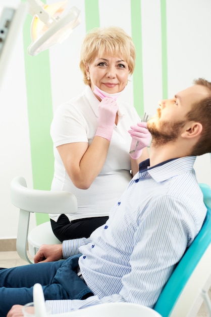 Woman dentist looking at the camera while giving dental treatment to male client of a modern dentistry.