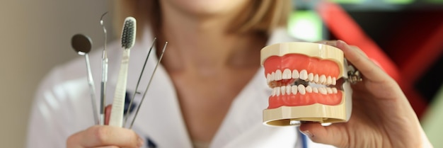 Woman dentist shows medical tools with toothbrush and teeth model concept of dentistry and