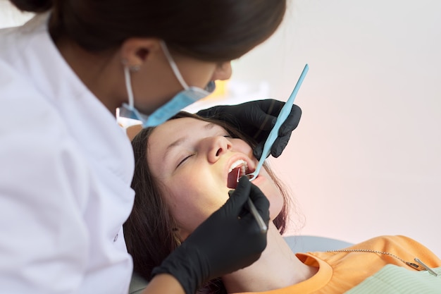 Woman dentist treating teeth to a patient sitting in dental chair using professional equipment