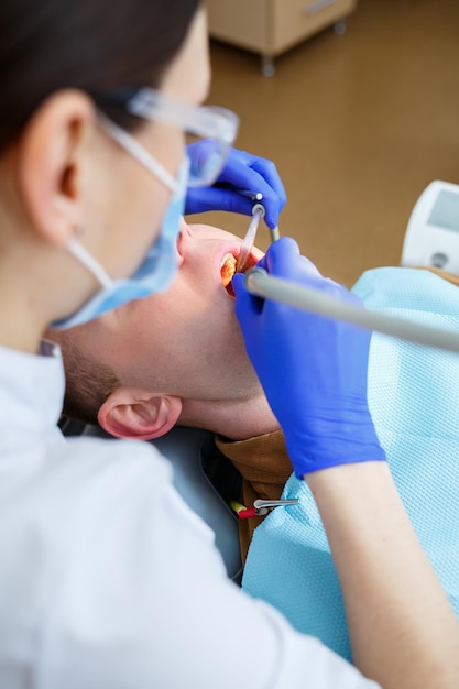 患者を治療している間の女性歯科医。医者は歯科医の椅子に座っている人の歯に歯科治療を行います。セレクティブフォーカス。