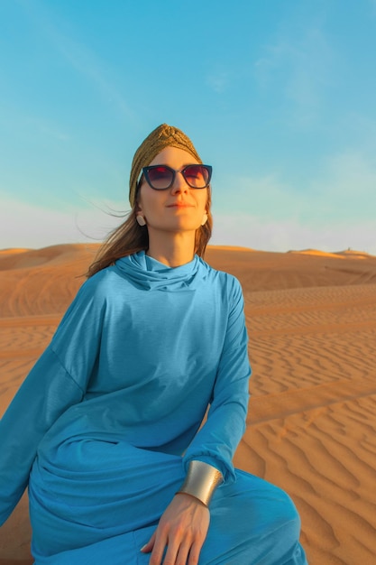 青いトップスと青いトップスを着た砂漠の女性が砂漠に座っています。