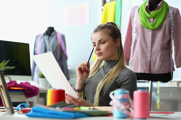 Woman designer are considering sketches of clothes at workplace in atelier