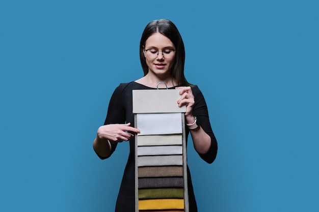Женщина-дизайнер-декоратор показывает вешалку с тканями на синем фоне