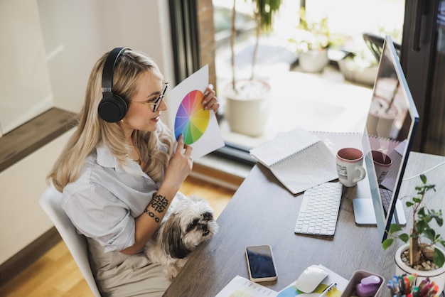 Woman designer having meeting online and having her pet dog in her lap to keep her company while working in comfort of her home.