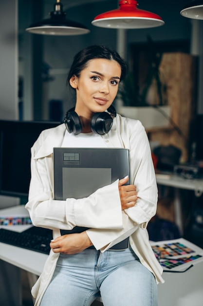 Woman designer with musical earphones standing in office holding folder