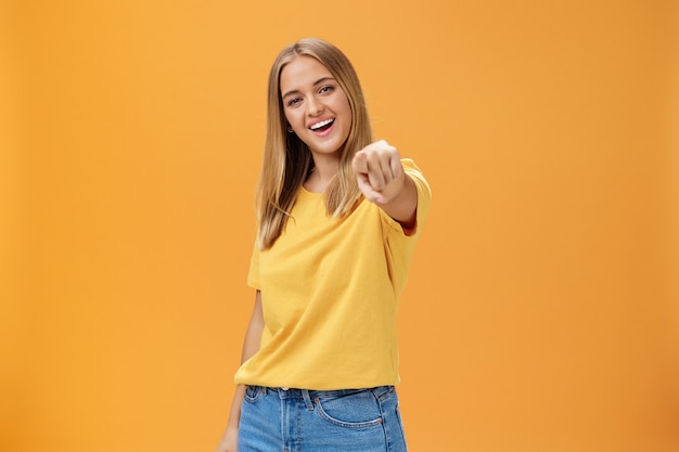 Woman directing at camera with index finger and smiling friendly as if talking to us standing amused...