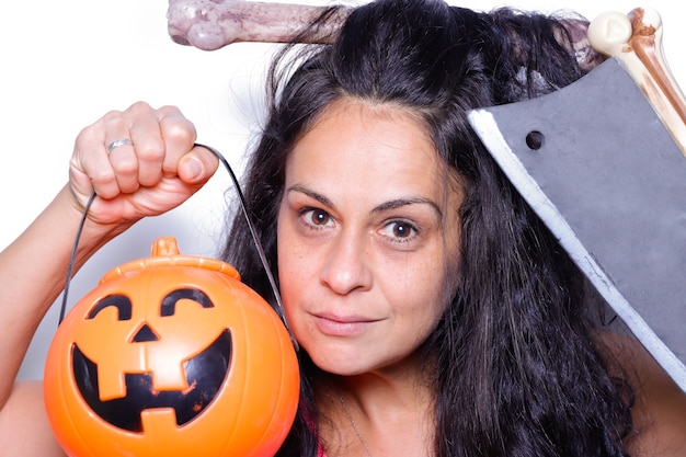 Woman disguised as a caveman on white background with pumpkin and ax in her hands and bone in her hair