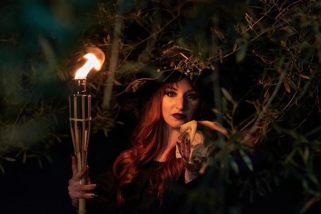 Woman disguised as a witch holding a flaming torch and a skull