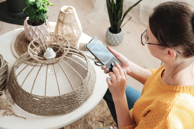 Woman diy blogger takes a photo on a mobile phone for diy blog in social media handmade jute rope lamp at home