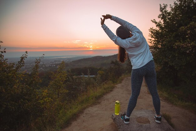 写真 女性は日の出の朝、街の上の丘の上で運動をする