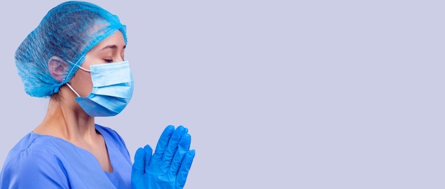 the woman doctor in blue medical uniform and mask with closed eyes is praying a quick recovery of th...