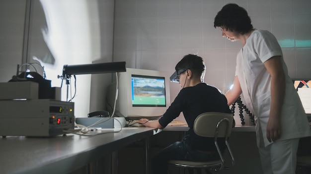 Woman doctor checks the boy's vision with the help of stereovideo virtual reality glasses, wide angle