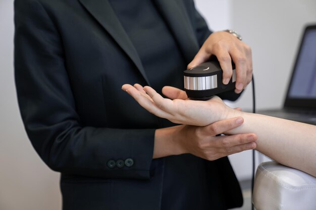 Woman doctor in a dark uniform suit is testing a patient's hand for her health statistic that show on the laptop monitor