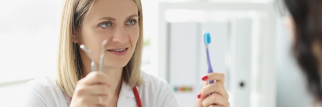 Woman doctor dentist shows patient toothbrush and dental instrument oral hygiene and dentistry