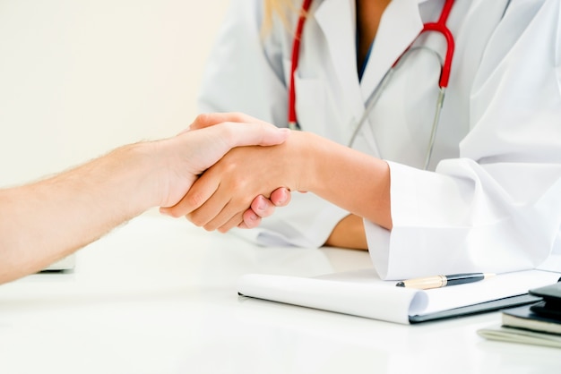 Woman doctor doing handshake with male patient in hospital office room.