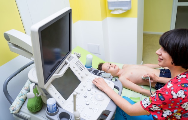 Woman doctor examining a boy with ultrasonic equipment at hospital.