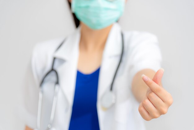 女医はミニハートの形で指で手を差し伸べ、コロナウイルスを保護するためにマスクを着用し、愛を与えることの象徴として手話を示し、注意と注意を払うことを約束するのがコンセプトです