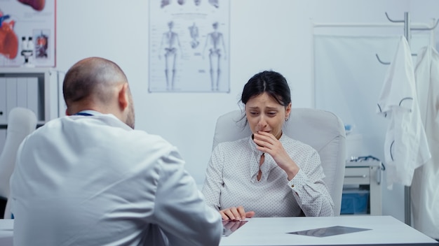 Woman at doctor hearing news about her incurable disease, she starts crying, is lost, depressed. Bad news about terminal patient. Cancer or other terminal ill concept