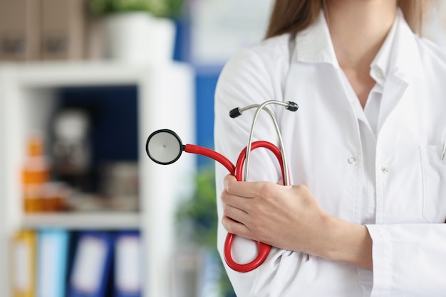 Woman doctor holding red stethoscope in clinic closeup