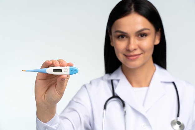 Woman doctor holding thermometer in her hand. Medical instrument for measuring body temperature, studio background. Focus at the thermometer