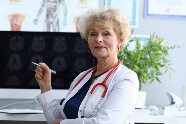 Woman doctor is sitting in an office holding pen in her hands and smiling.