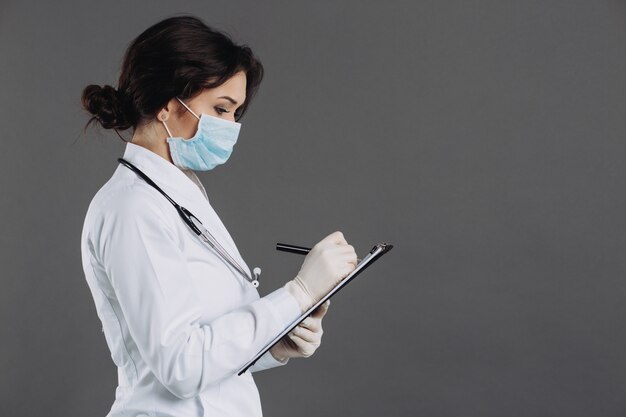 Woman doctor in mask and stethoscope holds folder and writes something in it related to coronavirus. Covid-19 concept