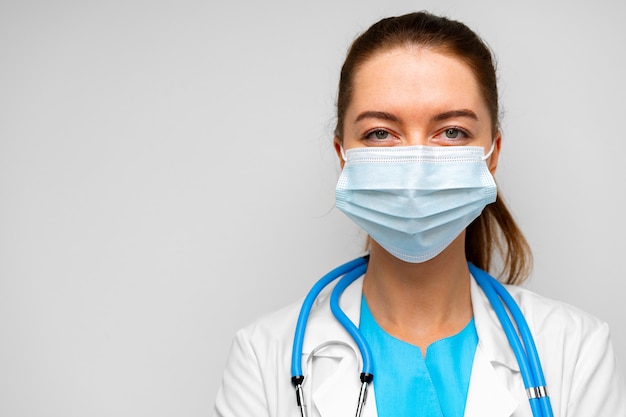 Woman doctor in medical mask standing against gray