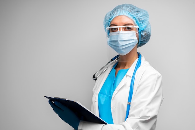 Woman doctor in medical mask standing with clipboard against gray portrait