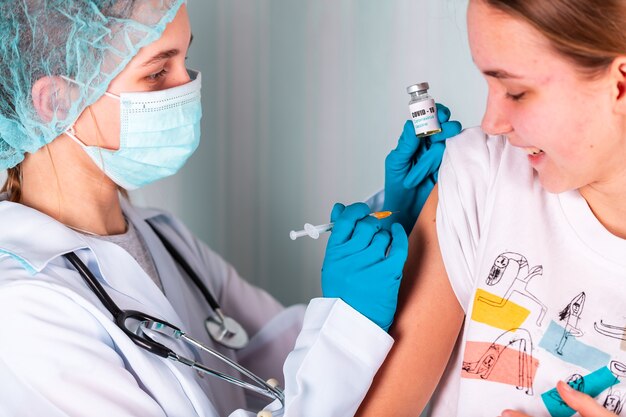 Woman doctor or nurse in uniform and gloves wearing face mask protective in lab, making an injecion holding vaccine bottle with COVID-19 Coronovirus vaccine label