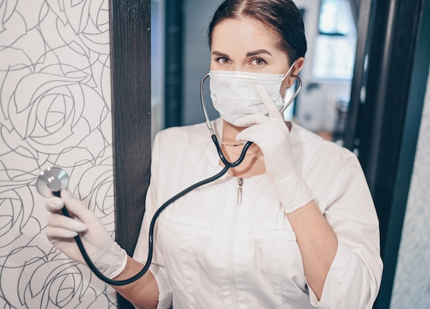 防護マスクと聴診器を身に着けている女性医師看護師は、呼吸チェック、コロナウイルス予防、コロナウイルスの拡散を停止するための衛生管理を行います。コロナウイルスのCovid-19コンセプトの汚染を回避する