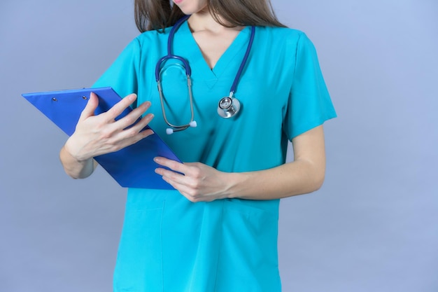 Женщина-врач-медсестра со стетоскопом смотрит на униформу буфера обмена на синем фоне
