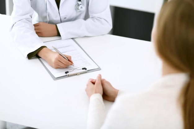 Woman doctor and patient sitting and talking at medical examination at hospital office closeup