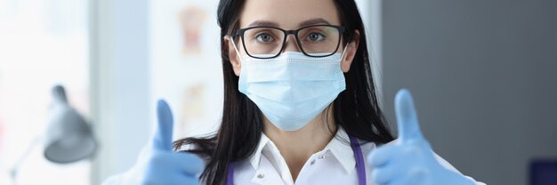 Woman doctor in protective gloves showing thumb up successful patient treatment concept