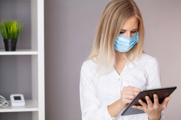 Woman doctor in protective mask working at tablet in office