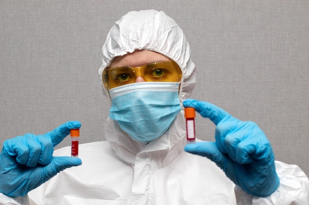 Woman doctor in protective suit and mask holding coronavirus infected blood sample test tube.